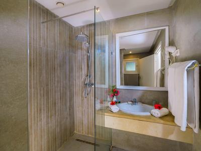 Moderní koupelna s béžovou sprchovou stěnou, skleněnou příčkou a umyvadlem s ručníky a dekoracemi.