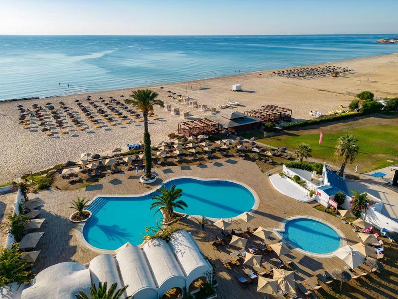 Letecký pohled na hotel s bazény, slunečníky a písečnou pláží s výhledem na moře.