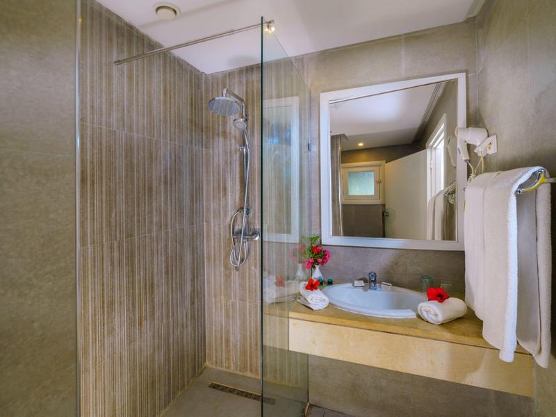 Moderní koupelna s béžovou sprchovou stěnou, skleněnou příčkou a umyvadlem s ručníky a dekoracemi.