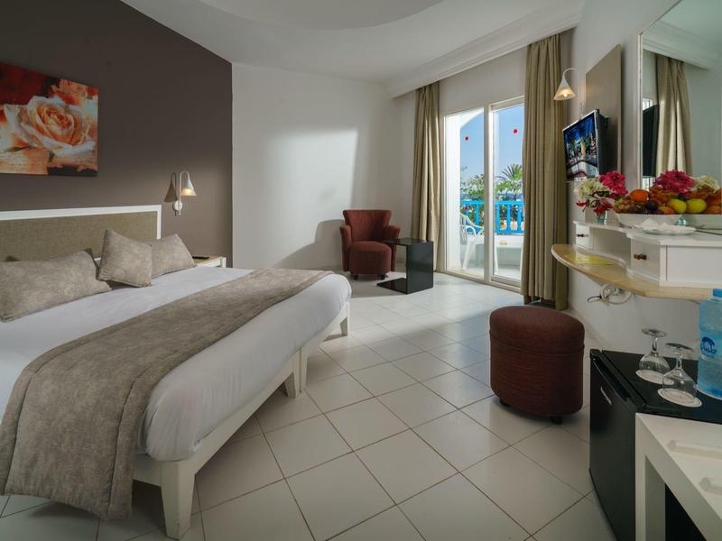 Moderně zařízený hotelový pokoj s velkou postelí, balkonem a posezením.