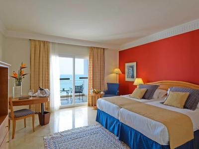 Pokój hotelowy z dużym łóżkiem, czerwoną ścianą i tarasem z widokiem na morze.