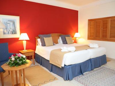 Elegancki pokój hotelowy z podwójnym łóżkiem, czerwoną ścianą akcentową i przytulnym miejscem do siedzenia.