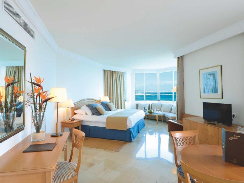 Jasny pokój hotelowy z podwójnym łóżkiem, biurkiem, oknem z widokiem na morze i nowoczesnym wystrojem.