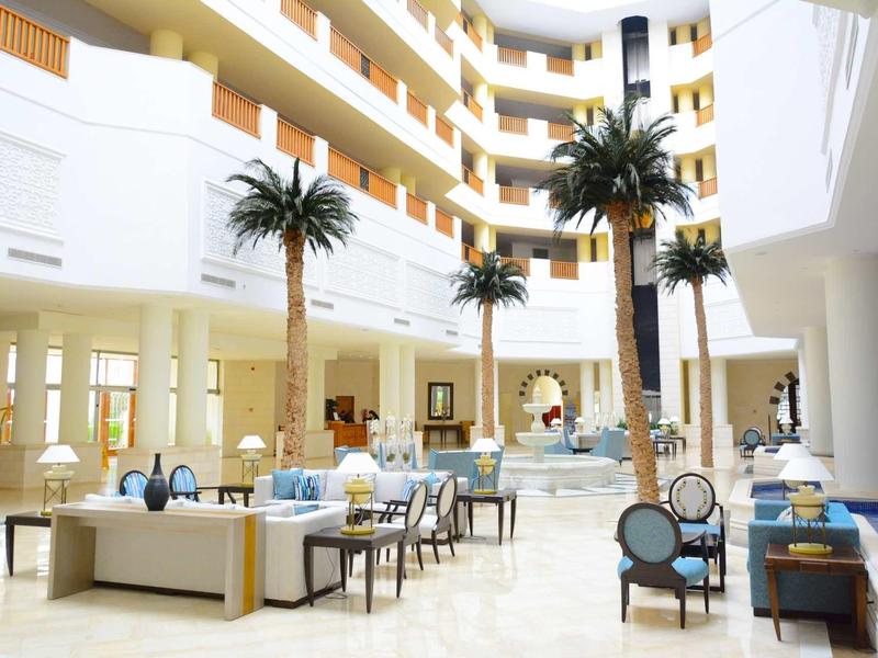 Jasna przestrzeń lobby hotelowego z miejscami do siedzenia i sztucznymi palmami.