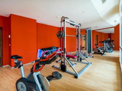 Nowoczesna siłownia z czerwoną ścianą, sprzętem cardio i siłowym na drewnianej podłodze.