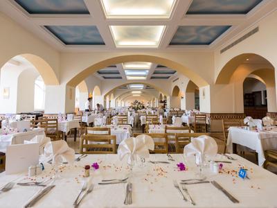 Großer Speisesaal mit cremefarbenen Wänden, Holzstühlen und weiß gedeckten Tischen unter gewölbter Decke.