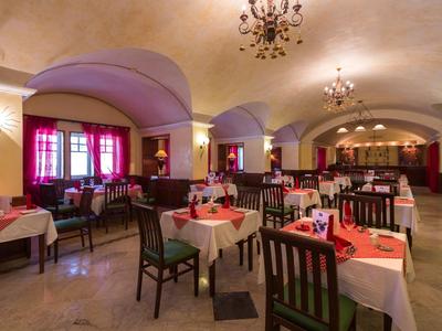 Elegancka restauracja z łukowymi sufitami, żyrandolami i starannie nakrytymi stołami w czerwono-białych barwach.