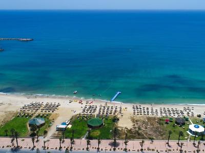 Słoneczna plaża z rzędami leżaków i parasoli przy przezroczystym, niebieskim morzu.