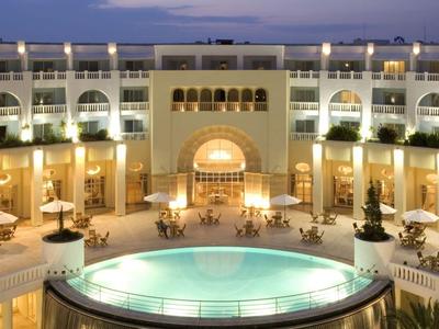 Luksusowy dziedziniec hotelowy z oświetloną fontanną i miejscami do siedzenia o zmierzchu.