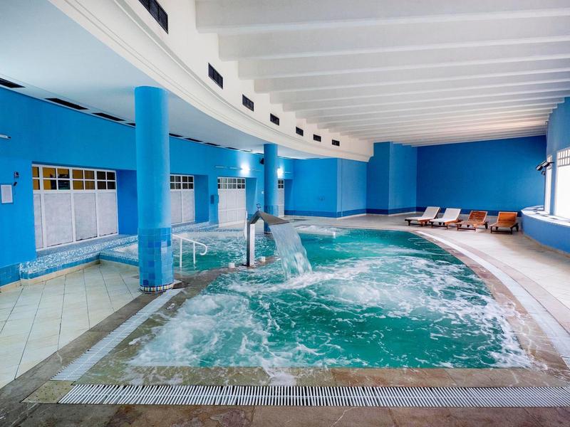 Kryty basen z bulgoczącą wodą i leżakami w niebieskim pokoju.