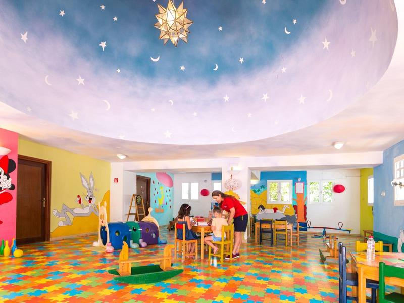 Kolorowy pokój zabaw dla dzieci z ozdobami z kreskówek, stołami, krzesłami i zabawnym oświetleniem sufitowym.