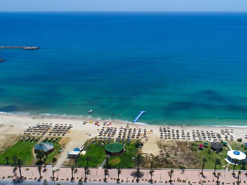 Słoneczna plaża z rzędami leżaków i parasoli przy przezroczystym, niebieskim morzu.