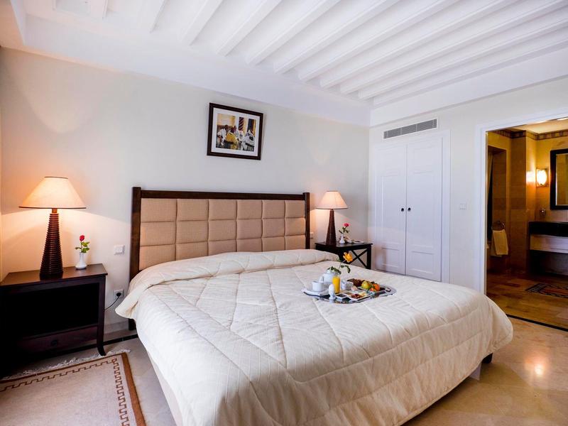 Przytulny pokój hotelowy z dużym łóżkiem, dwoma stolikami nocnymi i tacą z przekąskami.