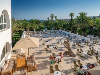 Groot terras met tafels, stoelen en parasols bij een tropisch hotel.
