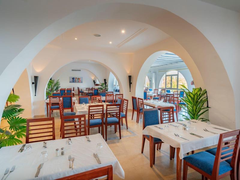 Licht restaurant met witte muren, houten tafels en blauwe stoelen in een gezellige sfeer.