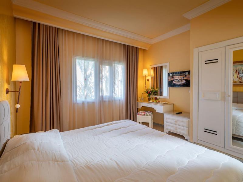 Gezellige hotelkamer met een groot bed, gordijnen en een verlichte kaptafel met spiegel.