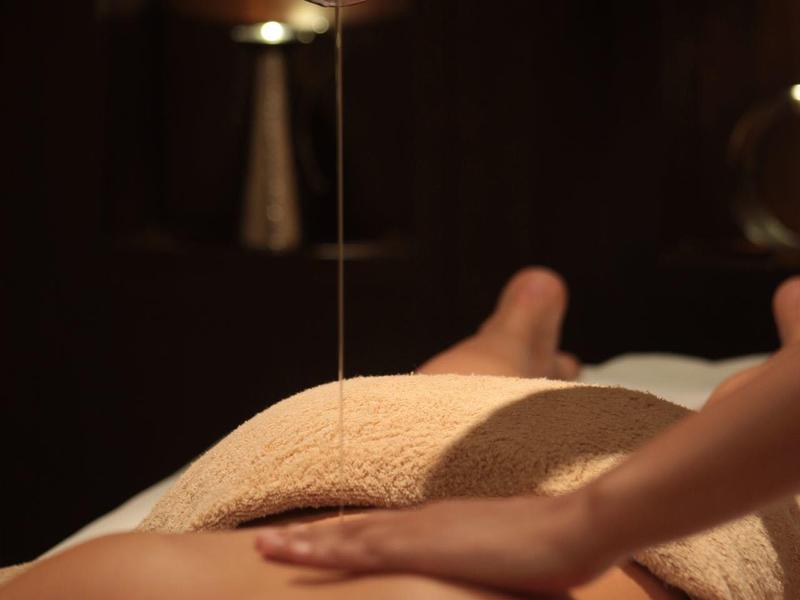 Relaksujący masaż pleców z gorącym olejem w przyciemnionym pokoju spa.