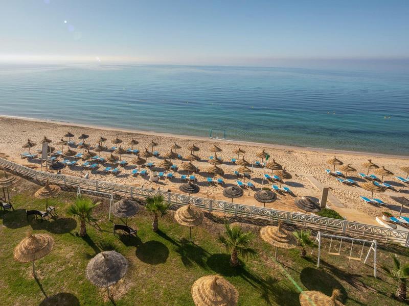 Widok na piaszczystą plażę z parasolami i leżakami obok spokojnego morza pod jasnym niebem.