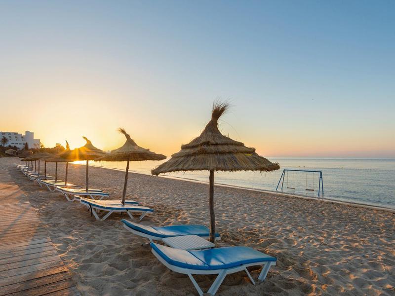 Puste leżaki plażowe z słomianymi parasolami o wschodzie słońca nad spokojnym morzem.