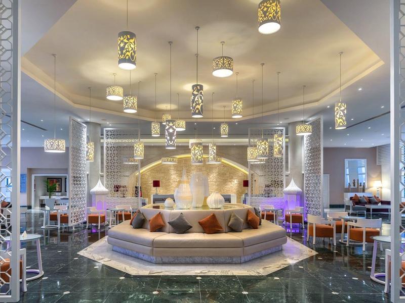 Nowoczesny i luksusowy salon hotelowy z jasnym wystrojem i miejscami do siedzenia wokół centralnej kolumny.