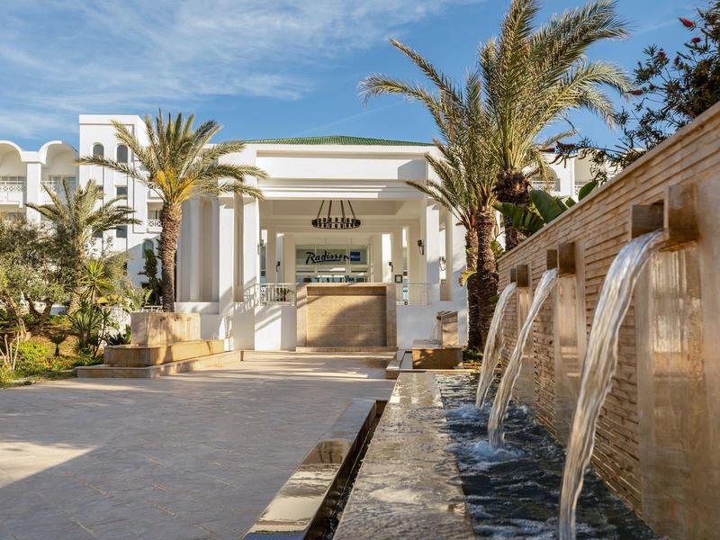 Hotel z basenem, fontannami wodnymi i palmami pod niebieskim niebem