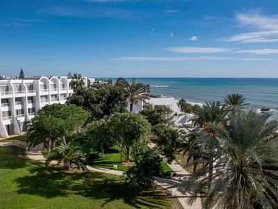 Hotelanlage mit weißen Gebäuden, Palmen und Blick auf das blaue Meer unter klarem Himmel.