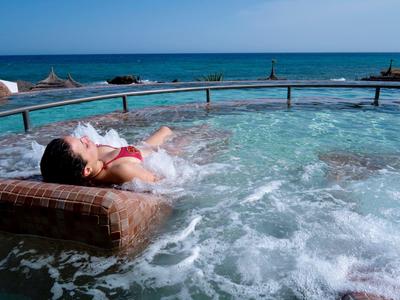 Uvolněná žena leží ve vířivce s výhledem na moře za slunečného dne.