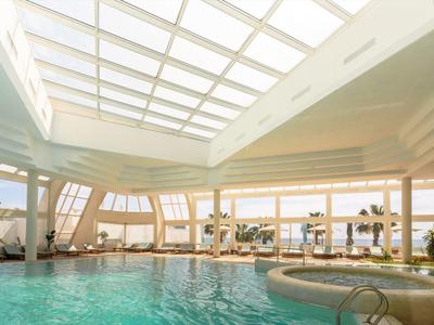 Vnitřní bazén s velkou prosklenou střechou a výhledem na palmy a moře