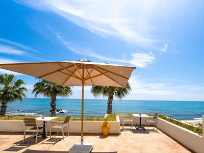 Terrasse mit Sonnenschirm und Blick auf das Meer mit Palmen unter blauem Himmel