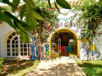 Eingang eines Hotels mit bunten Wandmalereien, umgeben von Grünpflanzen und Bäumen.