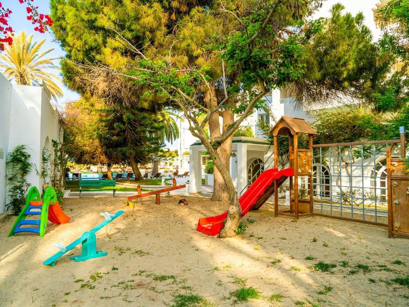 Dětské hřiště se pískovištěm, skluzavkou, houpačkou a prolézačkou na zahradě s stromy