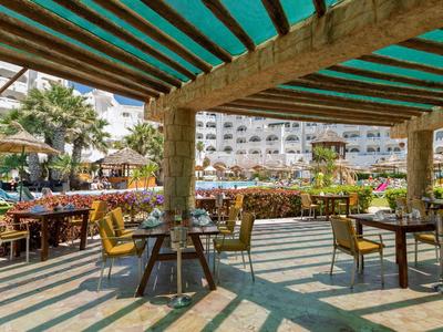 Terrasse extérieure d'hôtel avec tables, chaises et auvent vert par temps ensoleillé