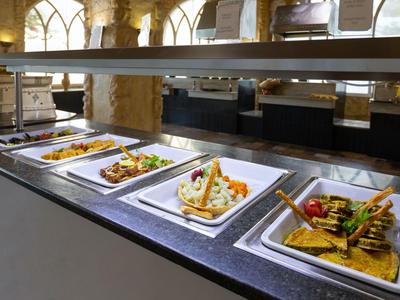Buffet met smakelijke gerechten en groenten in een lichte restaurant met stenen zuilen.