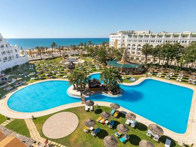 Velký bazén s deštníky mezi dvěma hotelovými budovami a výhledem na moře.