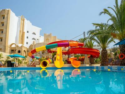 Waterpark met kleurrijke glijbanen, zwembad en palmbomen voor een hotelgebouw.