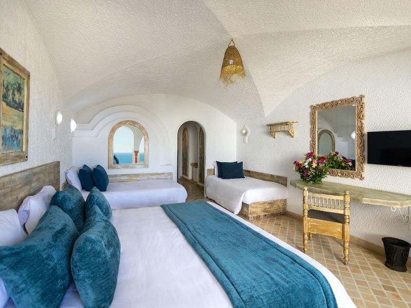 Světý hotelový pokoj se dvěma dvojlůžky, modrými polštáři a vintage nábytkem.