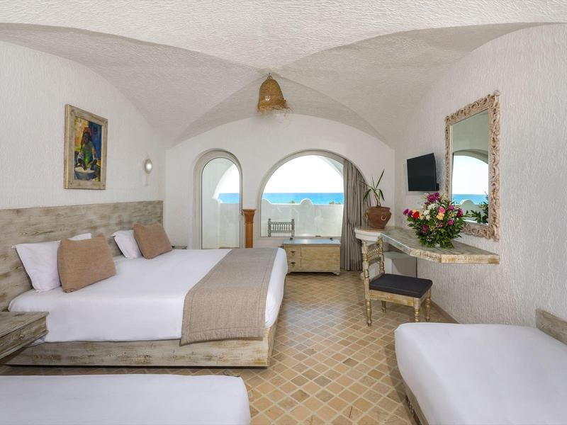 Svět hotelový pokoj s postelí, výhledem na moře a středomořskou výzdobou.