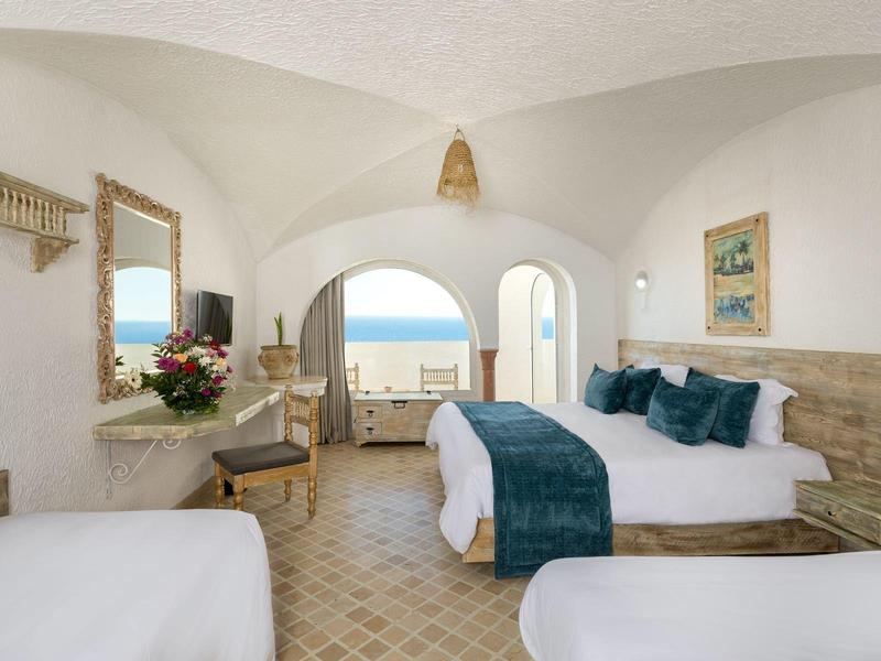 Světlý bílý pokoj s manželskou postelí, balkonem a výhledem na moře v hotelu.