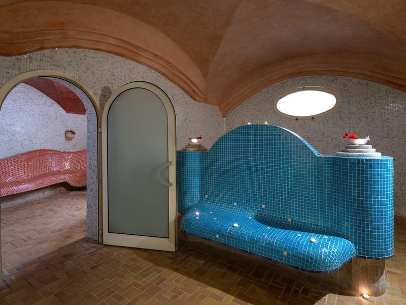 Pohodlná modrá lavička s malým stolkem v elegantní klenuté místnosti s terakotovými a mozaikovými zdmi.