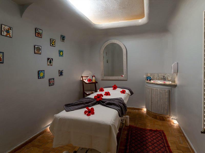 Klidná wellness místnost s masážním stolem, dekorativními květinami a měkkým osvětlením.