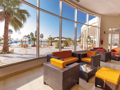 Lounge dell'hotel luminosa con grandi finestre che affacciano su palme e mare.