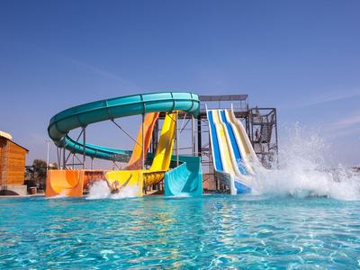 Vodní park s barevnými tobogány a čistým modrým bazénem pod jasnou oblohou.
