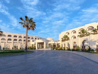 Velká hotelová budova s palmami pod jasně modrou oblohou při východu slunce.