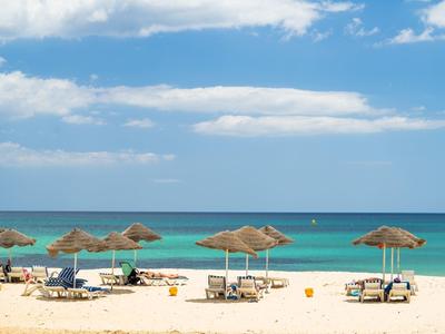 Spiaggia con lettini e ombrelloni sotto cielo blu e mare calmo.