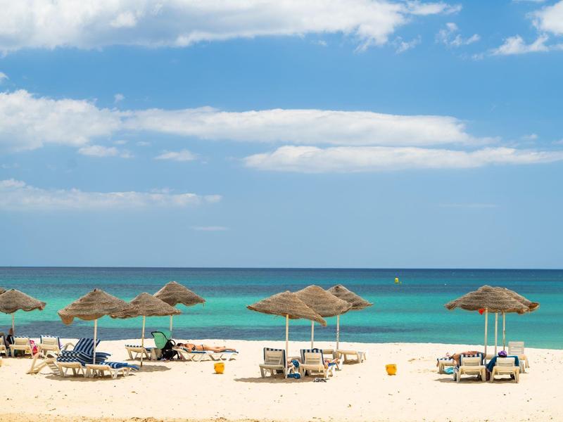 Spiaggia con lettini e ombrelloni sotto cielo blu e mare calmo.