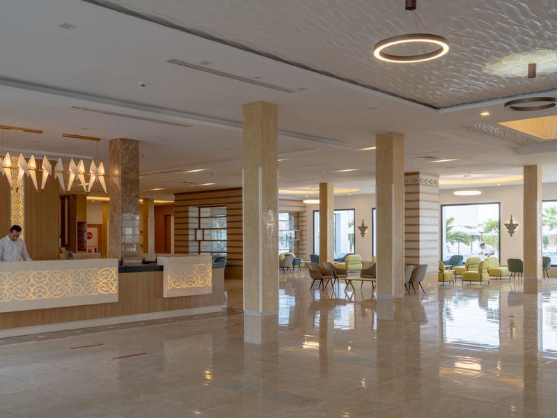 Ampia hall dell'hotel con reception, pavimento in marmo e aree salotto moderne.