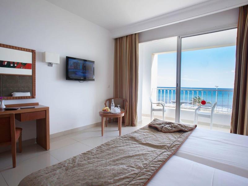 Camera d'hotel moderna con vista mare, letto matrimoniale, scrivania e balcone con zona salotto.