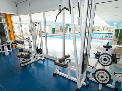 Salle de sport avec équipements d'entraînement et vue sur une piscine extérieure à travers de grandes fenêtres.