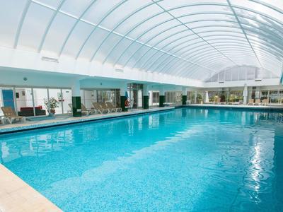 Großes, überdachtes Schwimmbecken mit hellem, gebogenem Glasdach und Sitzgelegenheiten innen.