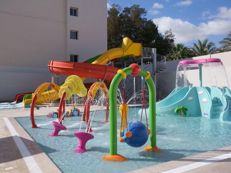 Kinderwasserspielplatz mit bunten Rutschen, Wasserspielen und flachem Becken bei Sonnenschein.